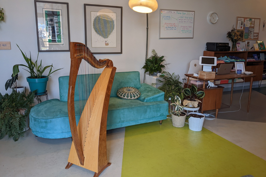 Melody's harp, named Dreamweaver, sits in the Purna Yoga 828 studio lobby. Soft lighting, lots of houseplants, and a big teal couch look inviting.
