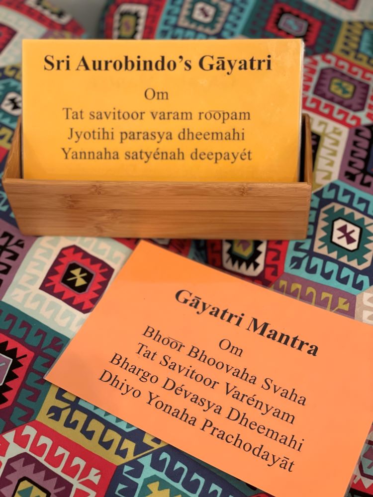 A photo of two laminated cards, one yellow in color and displaying the text of Gayatri, and the other orange and displaying the words to the Gayatri Mantra.