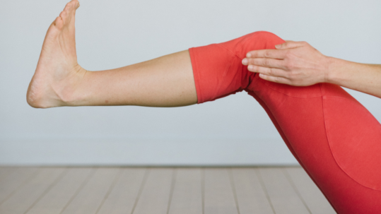 cropped photo showing just the lifted legs and flexed feet of a person wearing orange yoga leggings on a green mat