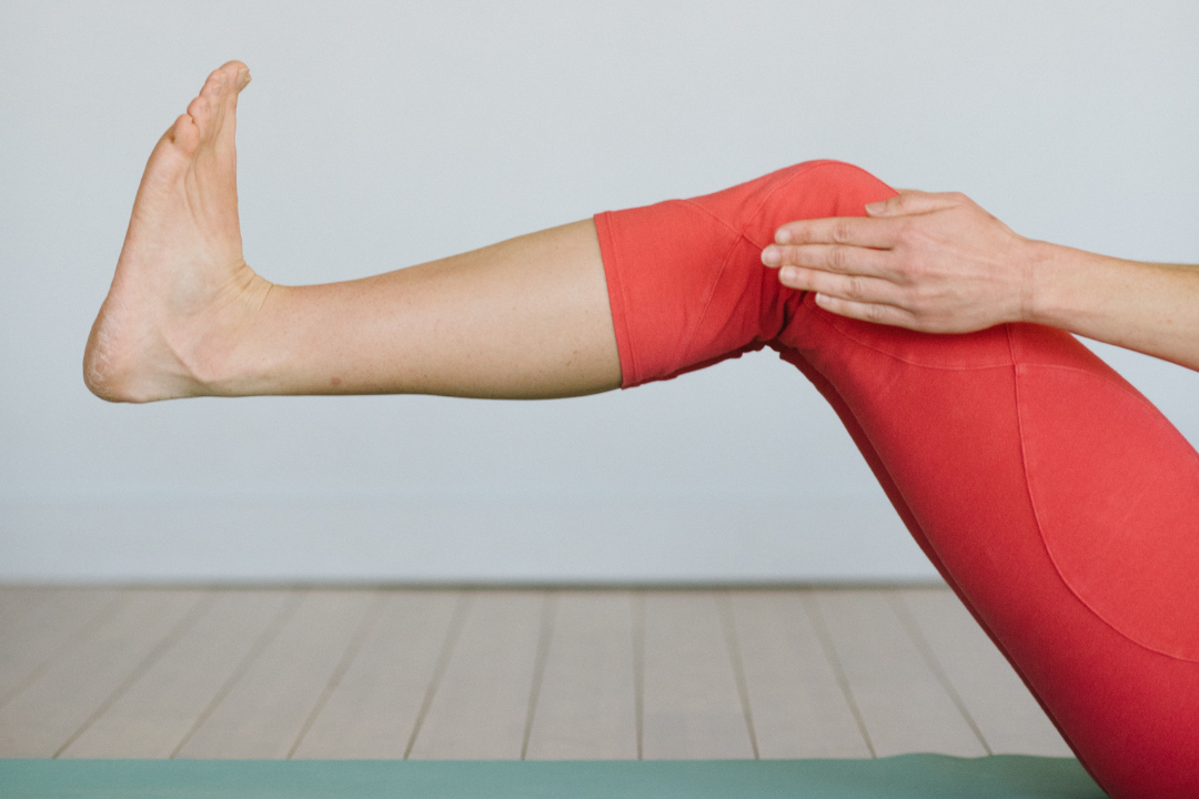 cropped photo showing just the lifted legs and flexed feet of a person wearing orange yoga leggings on a green mat